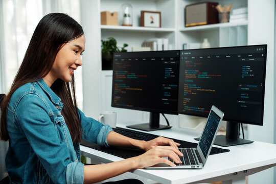 Smiling young Asian in IT developer creating with typing online information on laptop with coding program data of application, wearing jeans shirt. surrounded by safety analysis two screen. Stratagem.