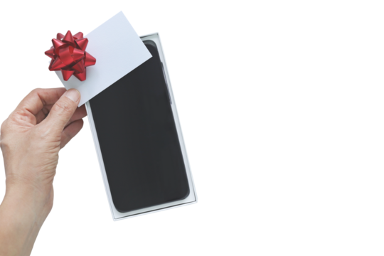 Men hand holding blank white card with red bow over new smartphone in box on transparent background. Top view flat lay of technology gift for Christmas or birthday with copy space. Holiday concept