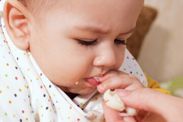Portrait of little baby boy eating food. Baby with a spoon in feeding chair. Cute baby eating first meal