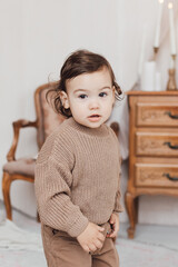 Portrait of a little baby. Cute boy in a brown sweater in a bright room