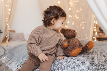 A small child, a toddler, is playing with a teddy bear. Trendy brown colors