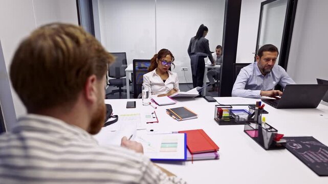 Diverse business coworkers are diligently working and collaborating at their desks in a modern, bright office.