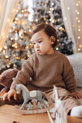 Little boy sitting on the bed in front of Christmas tree. Toddler playing with toys