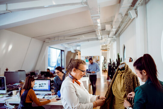 Young adult women smiling while designing dress in modern fashion studio