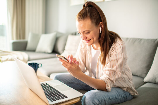 Young adult woman smiling while managing finances on smartphone at home