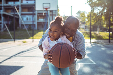 Adult father and child daughter laughing while playing basketball outdoors