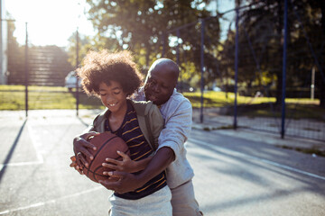 Adult father coaching child son, smiling on outdoor park basketball court