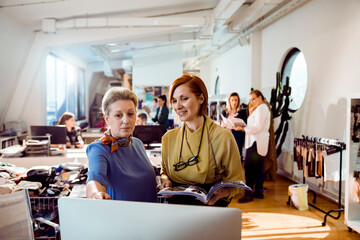 Adult women reviewing fashion designs at modern studio, focused and smiling