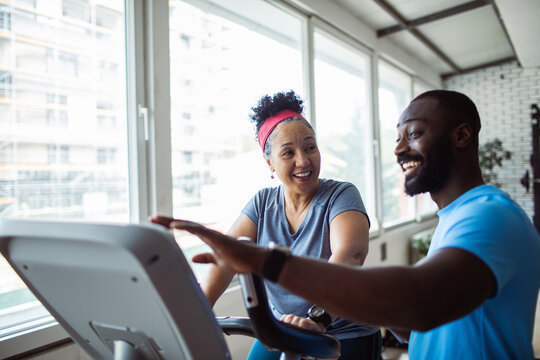 Mature adult woman smiling with trainer on exercise bike at gym