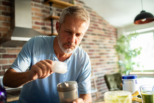 Mature man mixing protein shake in home kitchen, focused