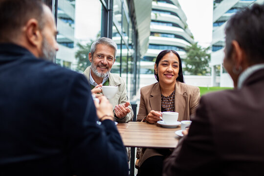 Adult and mature colleagues having coffee meeting in modern office courtyard, smiling