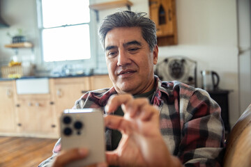 Mature man focused on smartphone at home kitchen