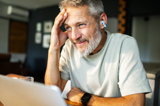 Smiling mature man using laptop and earbuds at home