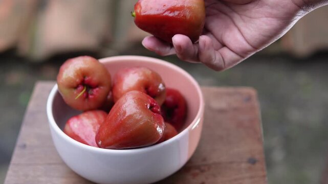 A person's hand taking a red water apple from a bowl. Fruit theme. Agriculture.