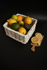 Organic lemons, limes, oranges and avocados placed in a white wicker basket. Fresh natural ingredients for healthy eating, cooking, wellness and immunity-related themes.