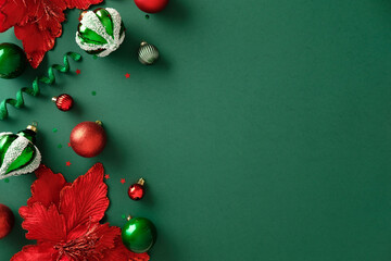 Christmas baubles and red poinsettia decorations on emerald green background. Flat lay. Top view.
