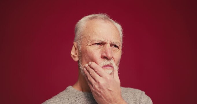 Sad senior man holding check having toothache looking at camera standing isolated on red background