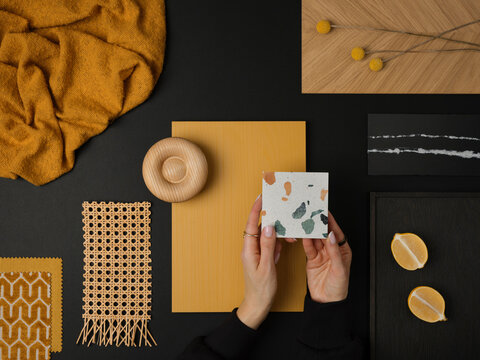 Modern material composition with mustard yellow, black, and wood elements, featuring terrazzo and woven rattan details.