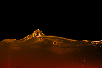 Golden brown liquid splash captured in motion with abstract wave shape on black background. Perfect for beverage, whiskey, coffee, or tea concept, emphasizing luxury, freshness, and energy.