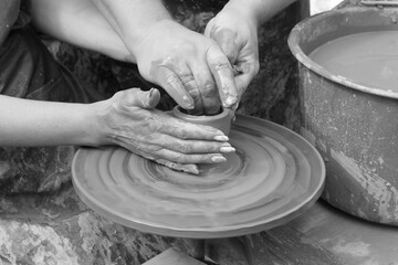 Retro style black and white photo depicting process of learning to make pottery with close-up of person's hands holding soft clay