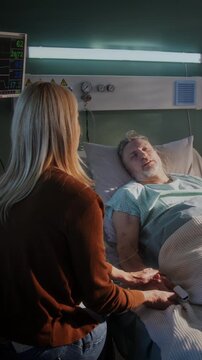 Elderly man rests on pillow and concerned woman sits nearby