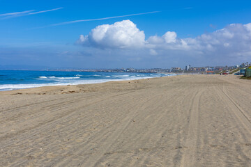Redondo Beach coastline with waves, sand, and residential houses under a blue sky.