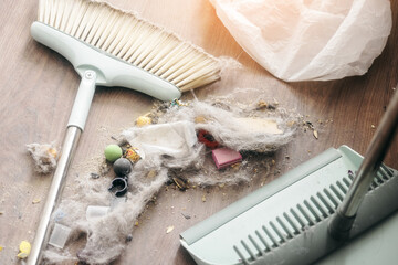 A close-up view of cleaning tools including a broom and dustpan, with dust and debris on a wooden floor, showcasing a messy cleaning situation.