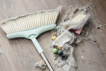 A broom and dustpan filled with dust, debris, and small objects on a wooden floor. Ideal for cleaning and home maintenance themes.