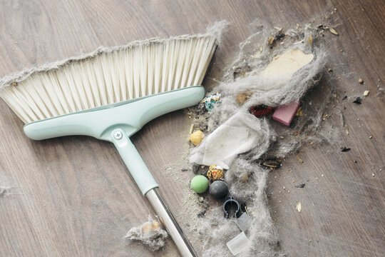A broom and dustpan filled with dust, debris, and small objects on a wooden floor. Ideal for cleaning and home maintenance themes.