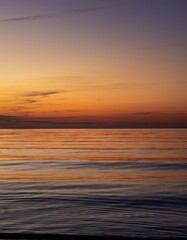 Obraz premium Vibrant orange and purple sunset sky reflects on calm ocean water with distant birds flying in a peaceful twilight scene