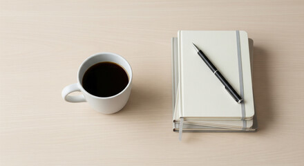 Overhead shot of a beautifully organized, minimalist coffee break setup on a light wooden table. Features a single white coffee cup, a small stack of professional notebooks, and a sleek pen.