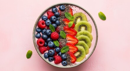 Overhead view of a pink smoothie bowl topped with blueberries raspberries sliced strawberries kiwi and chia seeds on a pink background