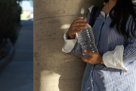 Student staying hydrated outdoors, holding a water bottle against a concrete column, symbolizing health, wellness, and responsible choices for active campus life - Powered by Adobe