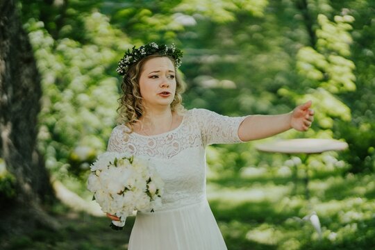 Bride with floral crown, wearing elegant white dress, passionately gestures while holding bouquet in lush green outdoor setting, capturing the essence of love and celebration - Powered by Adobe
