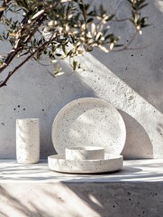 A collection of speckled ceramic plates, bowls, and a cup are artfully arranged on a textured concrete surface, bathed in dappled sunlight.