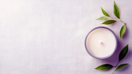 A top-down view of an unlit white candle in a glass jar, surrounded by fresh green leaves on a textured white surface.