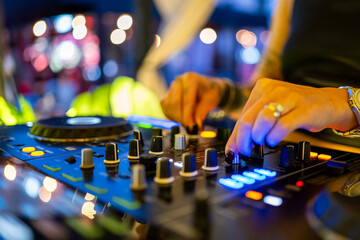 A female DJ performs an energetic live set, adjusting controls on a glowing mixer console amidst...