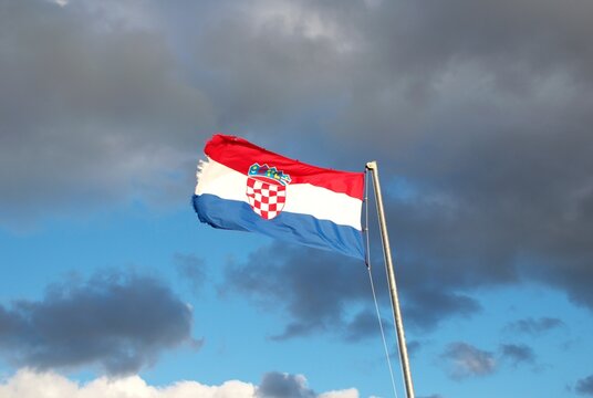 Vibrant Croatian flag with coat of arms waving in strong wind beneath a dramatic cloudy sky. Perfect for themes of patriotism, national identity, Europe, travel, and political or cultural symbolism.