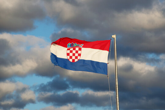 Vibrant Croatian flag with coat of arms waving in strong wind beneath a dramatic cloudy sky. Perfect for themes of patriotism, national identity, Europe, travel, and political or cultural symbolism.