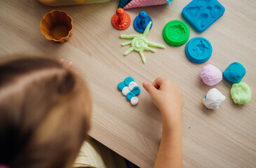 A little girl makes figurines out of colored airy plasticine, modeling dough. Hobbies for children's creativity, educational activities, development of fine motor skills of hands.