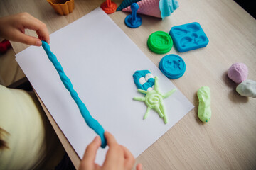 A little girl makes figurines out of colored airy plasticine, modeling dough. Hobbies for children's creativity, educational activities, development of fine motor skills of hands.