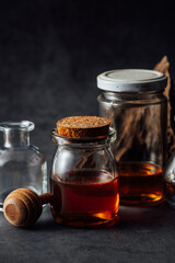 Glass jars filled with liquid and wooden honey dipper on dark background