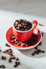 Red cup overflowing with roasted coffee beans on a textured surface
