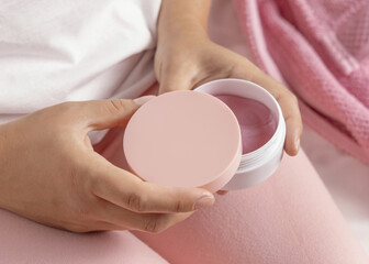 Closeup of woman in pink pyjamas holding cosmetic jar with blank lid in hands, mockup