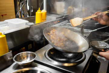 Chef stir-frying meat & vegetables in a hot, steaming wok in a professional commercial kitchen. Dynamic motion, high heat, and stainless steel surfaces