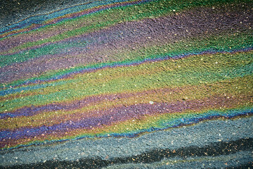 Oil slick spreads rainbow colors and iridescent texture across dark asphalt
