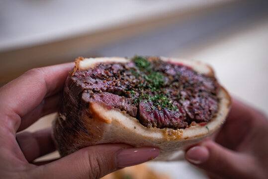 A person holds seared wagyu in a roasted bone marrow canoe with herbs at a Tokyo izakaya, juicy medium rare slices glisten as a travel diner savors bold flavor