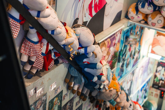 A narrow Tokyo anime shop staircase is lined with plush doll characters and walls of manga and idol posters, creating a playful tunnel of collectibles in Akihabara.