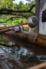 Obraz premium Close view of a temizuya at a Tokyo Shinto shrine shows a dragon spout, water drops, bamboo troughs, and metal ladles resting on wood in soft light.