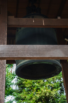 A large bronze bonsho hangs in a wooden belfry in Tokyo, close view shows patina and form, beams frame the bell, soft light suggests ritual use and quiet focus